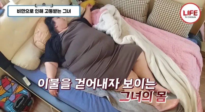 지팡이에 의지한 초고도비만 여성이 침대에 누워있는 모습