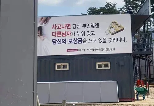 사고 시 보상금으로 부인 옆에 다른 남자가 있을 거라는 경고 문구가 적힌 부산국제아트센터 건립공사 현장 안전 표지판